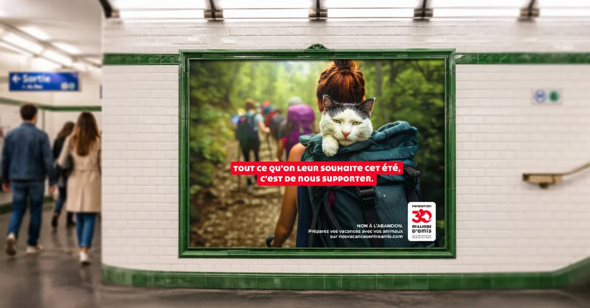 Panneau publicitaire dans le métro parisien affichant un autre visuel de la campagne Nos vacances entre amis, photo d'une marcheuse de randonnée vue de dos avec un chat blanc et noir installé dans son sac à dos, signature Tout ce qu'on leur souhaite cet été c'est de nous supporter, logo Fondation 30 Millions d'Amis, opération La Chose 2026
