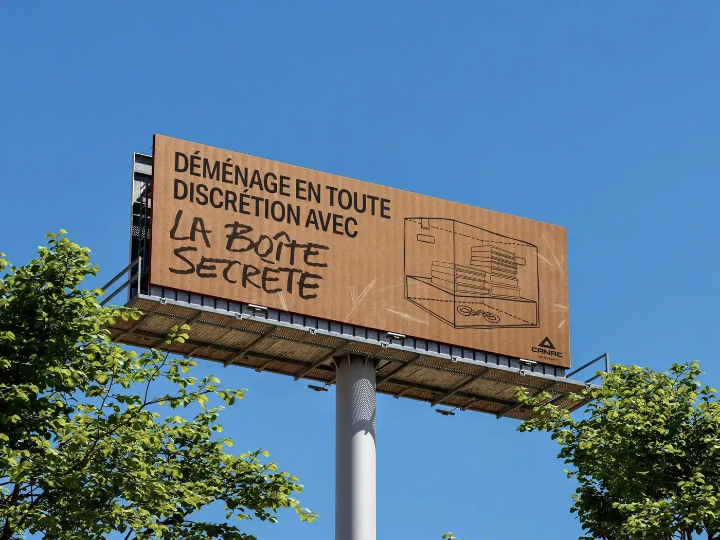La Boîte Secrète signée Canac et LG2 dévoilée le 15 juin 2026, carton de déménagement standard kraft uni vu de face avec couvercle ouvert montrant le faux fond en train d'être soulevé pour révéler un compartiment caché sous la base, scène d'intérieur québécois beige et lumineux, dispositif disponible dans les 37 magasins Canac à partir de la mi-juin