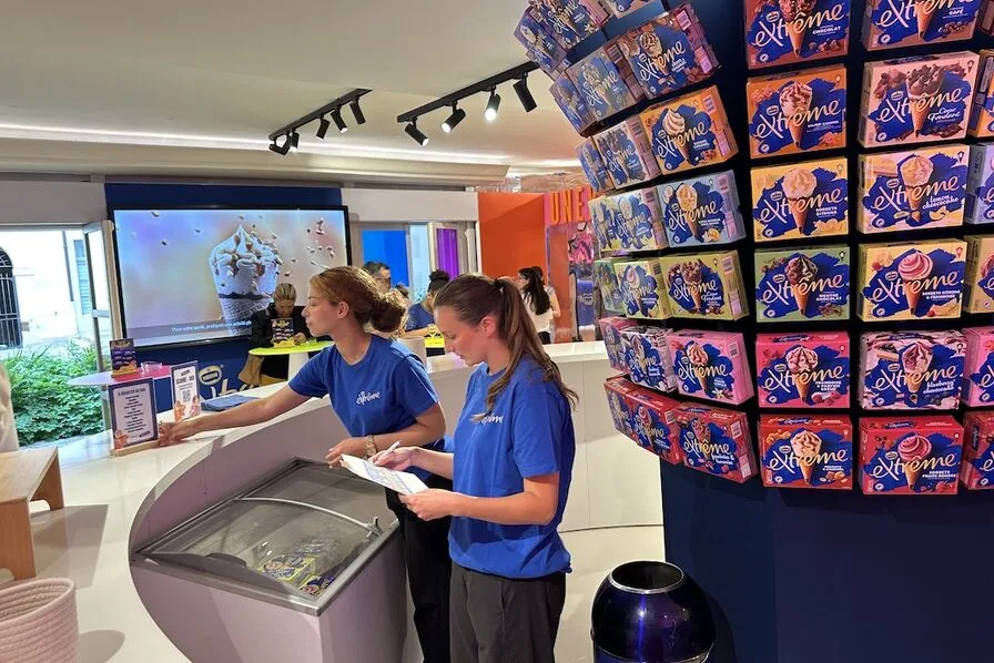 Intérieur du pop-up Personality Lab d'Extrême au 18 rue de Turenne dans le Marais à Paris, mur entier de cônes glacés exposés en présentoir, hôtesses bleues à l'accueil du bar à glaces, dispositif documenté par LSA Conso le 2 juin 2026