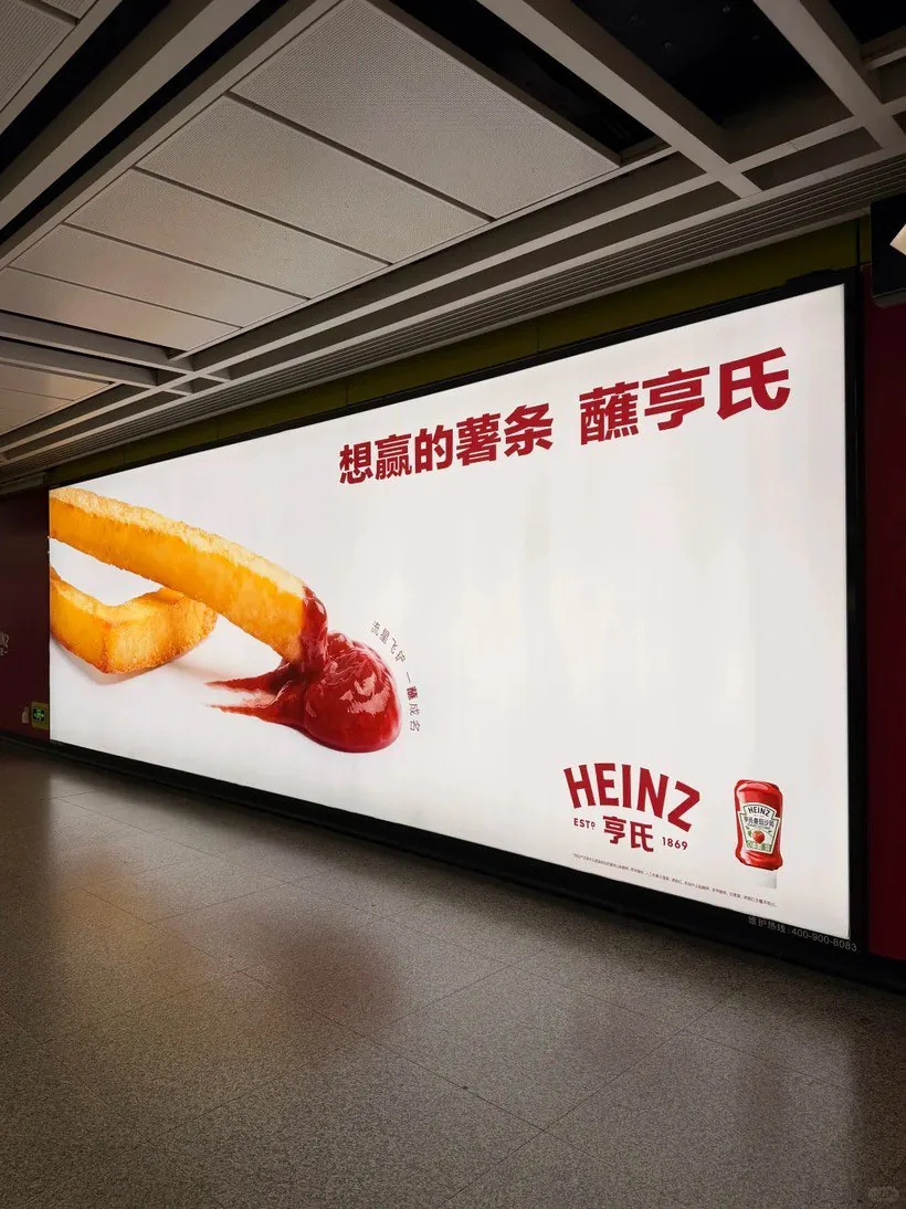 Deuxième visuel de la campagne Heinz dans le métro de Canton en juin 2026, plan rapproché d'une frite plongeant dans une éclaboussure de ketchup avec la bouteille emblématique Heinz Est. 1869 visible à droite, baseline en chinois et logo dans le coin, affichage indoor lumineux sur fond blanc