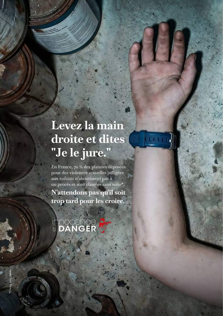 Deuxième visuel de la campagne Innocence en Danger Babel du 18 juin 2026, plan large d'une chambre d'enfant abandonnée à la lumière froide d'un matin gris, peluche en gros plan sur un parquet brut taché de poussière et de débris de plâtre, accroche manuscrite rouge Levez la main droite et dites Je le jure en haut du visuel, signature en bas N'attendons pas qu'il soit trop tard pour les croire, logo association en bas à droite