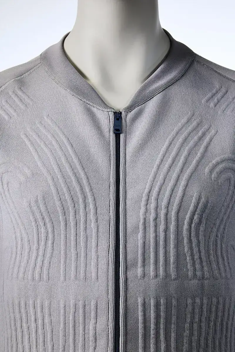 Détail technique de la Liquid Cooling Garment Prada Axiom dévoilée le 16 juin 2026, gros plan sur le réseau de tubes transparents tissés dans le textile blanc à hauteur du genou de l'astronaute, jonction en titane des conduits d'arrivée et de sortie d'eau visible, broderie Prada Sport discrète en argent sur la couture latérale, image studio en lumière naturelle