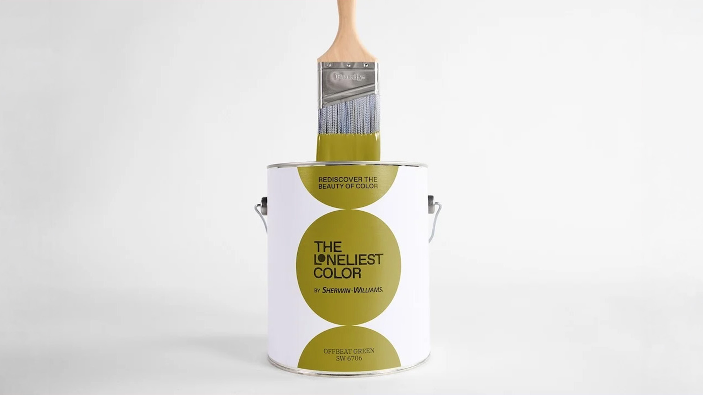 Photographie de studio sur fond blanc cassé du pot édition limitée The Loneliest Color 2026 signé Sherwin-Williams dévoilé le 10 juillet 2026, pot cylindrique métallique blanc à anse métallique portant l'étiquette design composée de trois cercles chartreuse olive alignés verticalement au centre desquels s'affichent en noir The Loneliest Color by Sherwin-Williams et Offbeat Green SW 6706, un large pinceau Purdy en bois clair plongé dans le pot avec les poils enduits d'une épaisse couche de peinture chartreuse dégoulinant sur le bord, éclairage doux tirage e-commerce